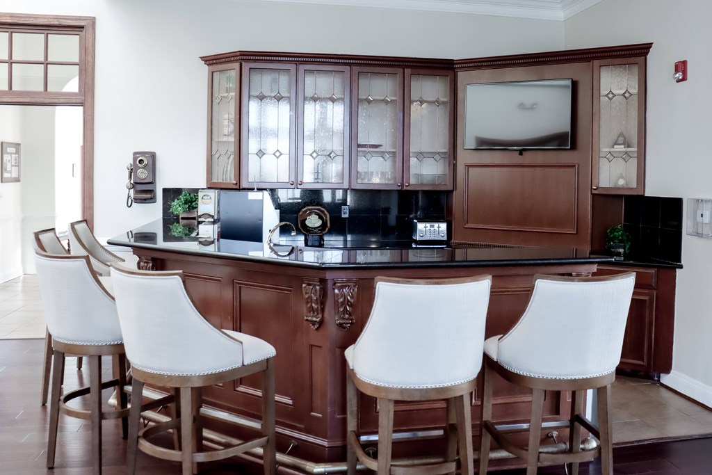 a bar with white chairs in a living room with a wooden cabinet at Broadlands Apartments in Ashburn, VA